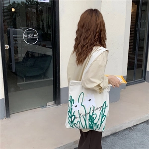 Outdoor street view of a beige canvas tote bag with floral prints worn over the shoulder