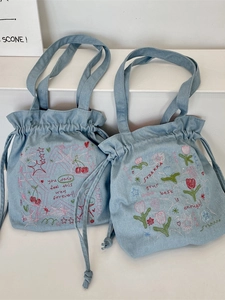 Light blue denim drawstring tote bag with colorful embroidery and a wide handle