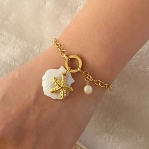 Golden starfish and shell charm bracelet with a white pearl on a soft background