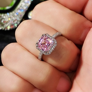 Detailed view of square pink gemstone ring with halo diamonds on a hand