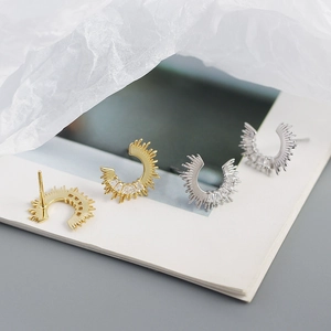 Macro detail of gold and silver sunburst C-shaped earrings with inlaid zircon on book