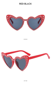 Detail view of heart-shaped sunglasses with red rhinestone frames and dark lenses