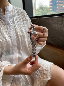 Detail of a pink dial lady watch with silver metal strap and calendar window on wrist