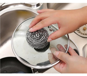 Person using a stainless steel scouring pad to clean a glass pot lid in the kitchen sink