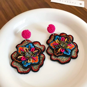 Close-up of intricate embroidered fabric flower earrings with beads and crystal detail