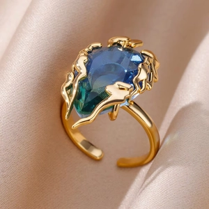 Detailed close-up of a gold ring featuring a large heart-shaped teal gemstone on pink silk
