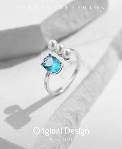 Detail of silver open ring with blue oval gemstone and three pearls on stone surface