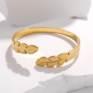Minimalistisches goldfarbenes Feder-Manschettenarmband aus Edelstahl auf Stein