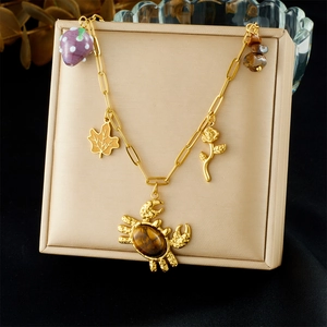 Gold charm necklace with tiger eye crab, rose, leaf, and strawberry pendants on display