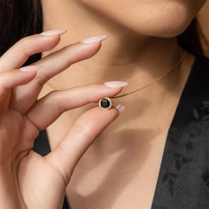 Gold necklace with round black stone pendant and halo of white diamonds on a model