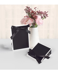 Détail d'un sac cadeau noir élégant avec bord blanc et nœud en ruban de satin noir