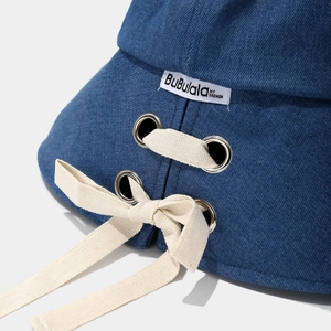 Detail eines dunkelblauen Denim-Anglerhuts mit Metallösen und dekorativer Baumwollschleife