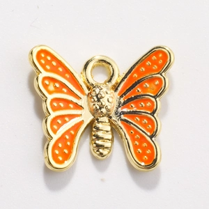 Macro detail of an orange enamel butterfly pendant with a golden alloy metal frame