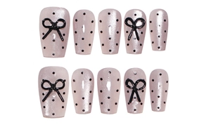 Detail of pink pearl press-on nails with black polka dots and 3D bow decorations