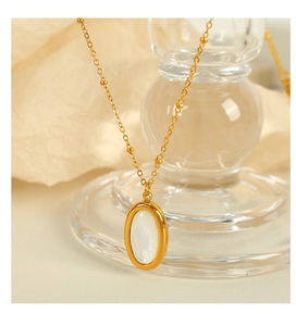 Macro detail of gold oval pendant necklace with white shell inlay and beaded chain