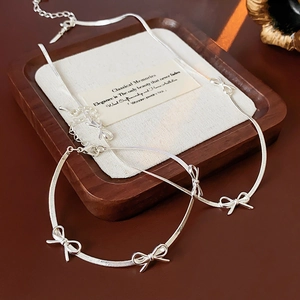 Detailed view of silver bow-knot necklace and bracelet set on a wooden display tray