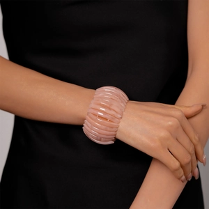Détail d'un large bracelet en acrylique rose avec texture marbrée au poignet du mannequin