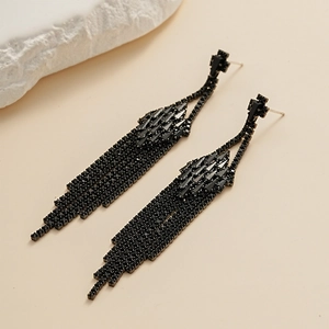 Gros plan détaillé de boucles d'oreilles à pompons noirs serties de strass sur fond beige
