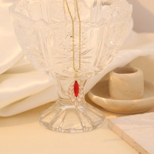 Close-up of gold leaf pendant with red and white marquise zircon on a glass rim