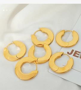Detailed view of wide gold hoop earrings with polished finish on white satin fabric