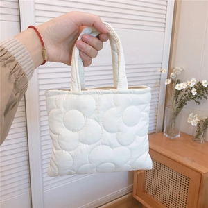 Dettaglio di una borsa imbottita trapuntata bianca con motivo floreale e zip in mano