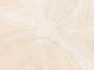 Nahaufnahme der weißen Kokosnuss-Stickerei auf dem beigen Boho-Maxikleid aus Leinen