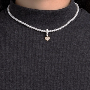 Close-up of pearl necklace with gold heart pendant worn on dark grey turtleneck