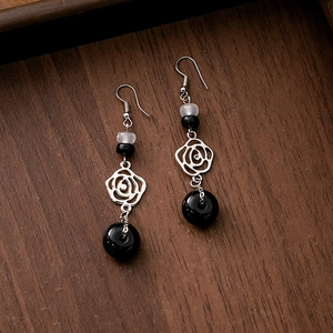 Detail of beaded tassel earrings with black beads and hollow silver rose on wood texture