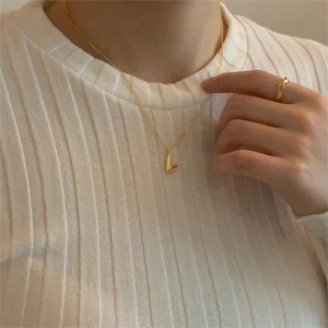 Macro detail of a minimalist gold curved pendant necklace worn on a white sweater