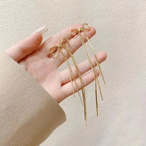 Eleganti orecchini a fiocco dorati con lunghe nappe su uno sfondo stile minimalista
