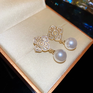 Macro shot of gold floral earrings with zircon stones and hanging pearls in a box