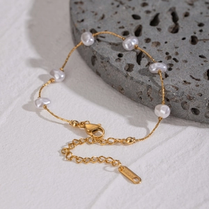 Gold stainless steel chain bracelet with irregular pearls on a grey volcanic rock