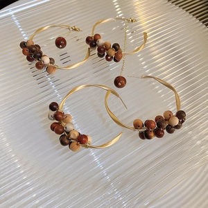 Detail view of gold twisted C-shaped earrings with sandalwood beads on glass tray