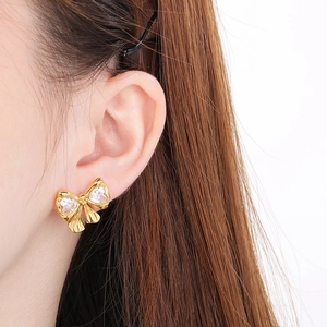 Close-up of golden bow earrings with heart-shaped cubic zirconia worn by a model