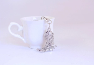 Macro shot of silver rhinestone-studded denim boot keychain next to a white teacup