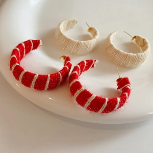 Detail of red striped and beige woven C-shaped earrings on a white ceramic tray