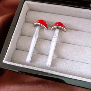 Chic red mushroom pearl drop earrings with silver pins displayed on silk fabric