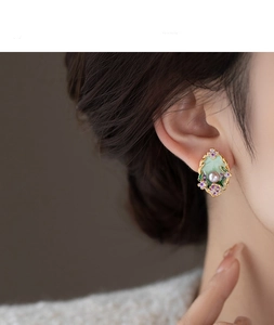 Detail of floral pearl stud earring in green enamel and gold finish on model