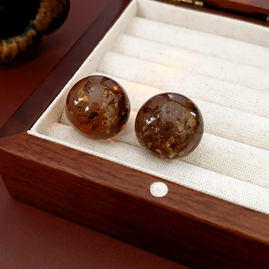 Detailed close-up of amber resin sphere earrings with embedded gold foil in a jewelry box