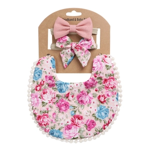 Detail of floral baby bib with lace trim and matching bow headbands on display card