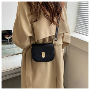 Classic black saddle bag with gold metal buckle worn by model in a stylish trench coat