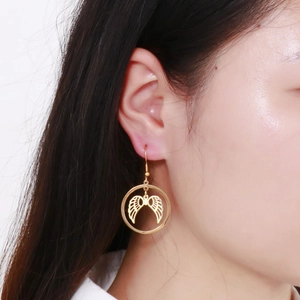 Detailed close-up of gold hollow angel wing circular drop earrings on a female model