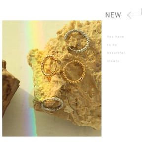 Artistic close-up of gold and silver hammered hoop earrings on textured rock surface