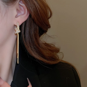 Detail of gold-plated knot earrings with zircon tassels worn on a model in a black suit