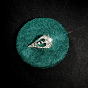 Macro shot of sparkling crystal-embedded silver V-shape open ring on green velvet