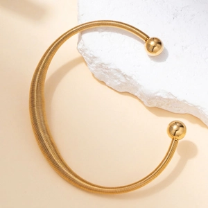 Close-up of golden flexible spring torque necklace with round metal beads on stone