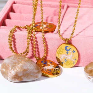 Close-up of three gold rabbit tarot necklaces on pink velvet and smooth stones