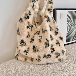 Detail of soft floral plush tote bag with a woven logo tag on a textured beige surface