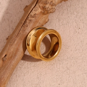Vue artistique d'une bague large dorée minimaliste posée sur une branche en bois naturel