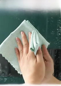 Gros plan d'un chiffon de nettoyage vert à écailles de poisson essuyant du verre mouillé